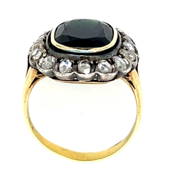 A vintage-style ring featuring a large, cushion-cut black gemstone in a gold bezel setting, surrounded by a halo of small clear stones on a gold band, set against a plain white background.