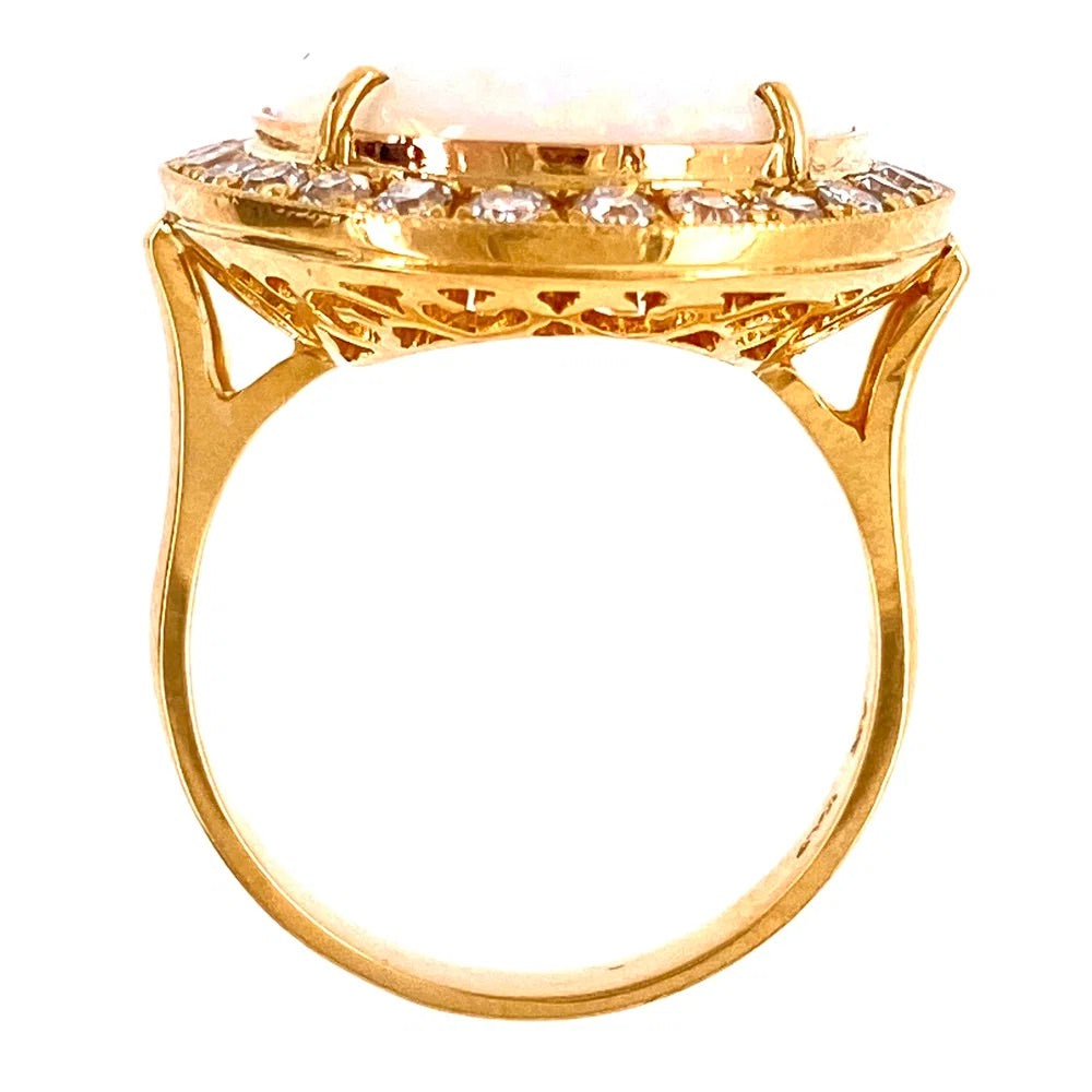 A yellow gold ring featuring a large oval pale pink stone in a prong setting, surrounded by a halo of small clear stones, shown against a plain white background.