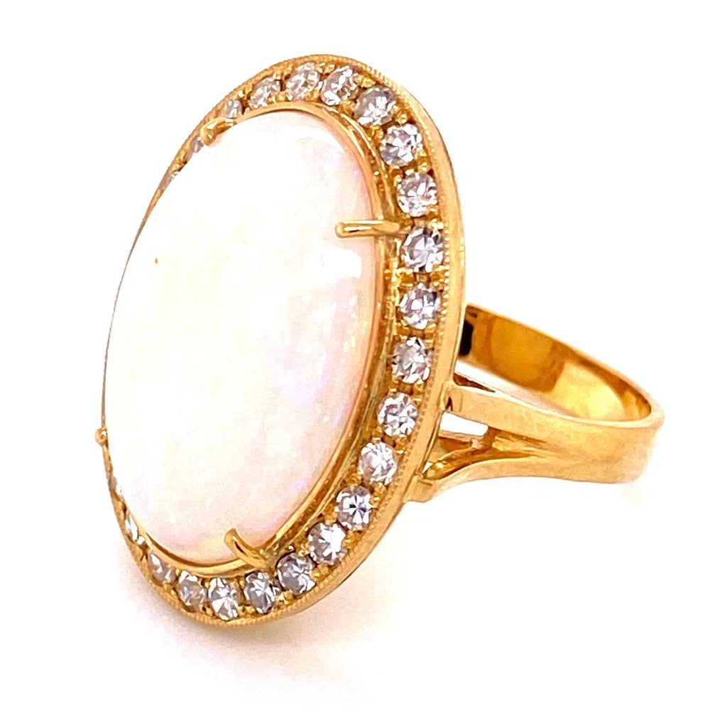 A gold ring featuring a large oval white opal center stone surrounded by a halo of small clear stones, shown on a plain white background.