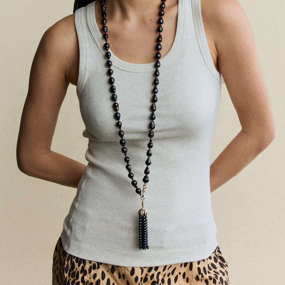 Woman wearing a gray tank top and leopard print pants with a long black beaded necklace.