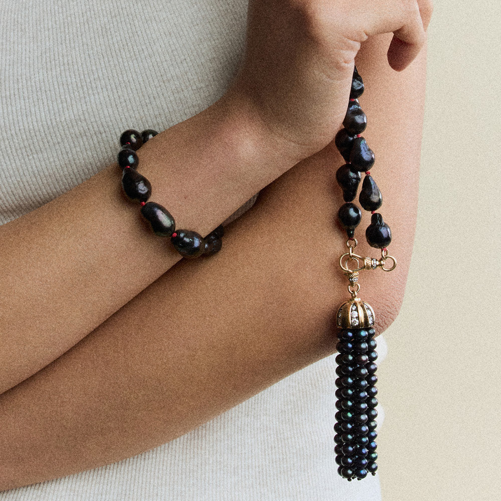 Person wearing a black beaded necklace with tassel on a neutral background