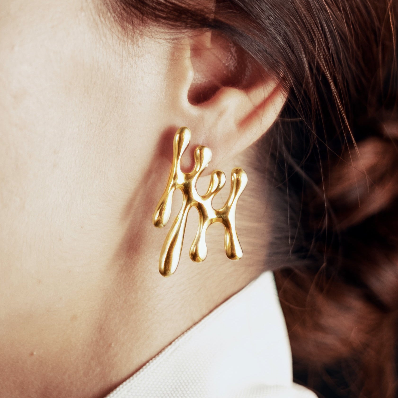 Gold earrings worn by a person with a blurred background