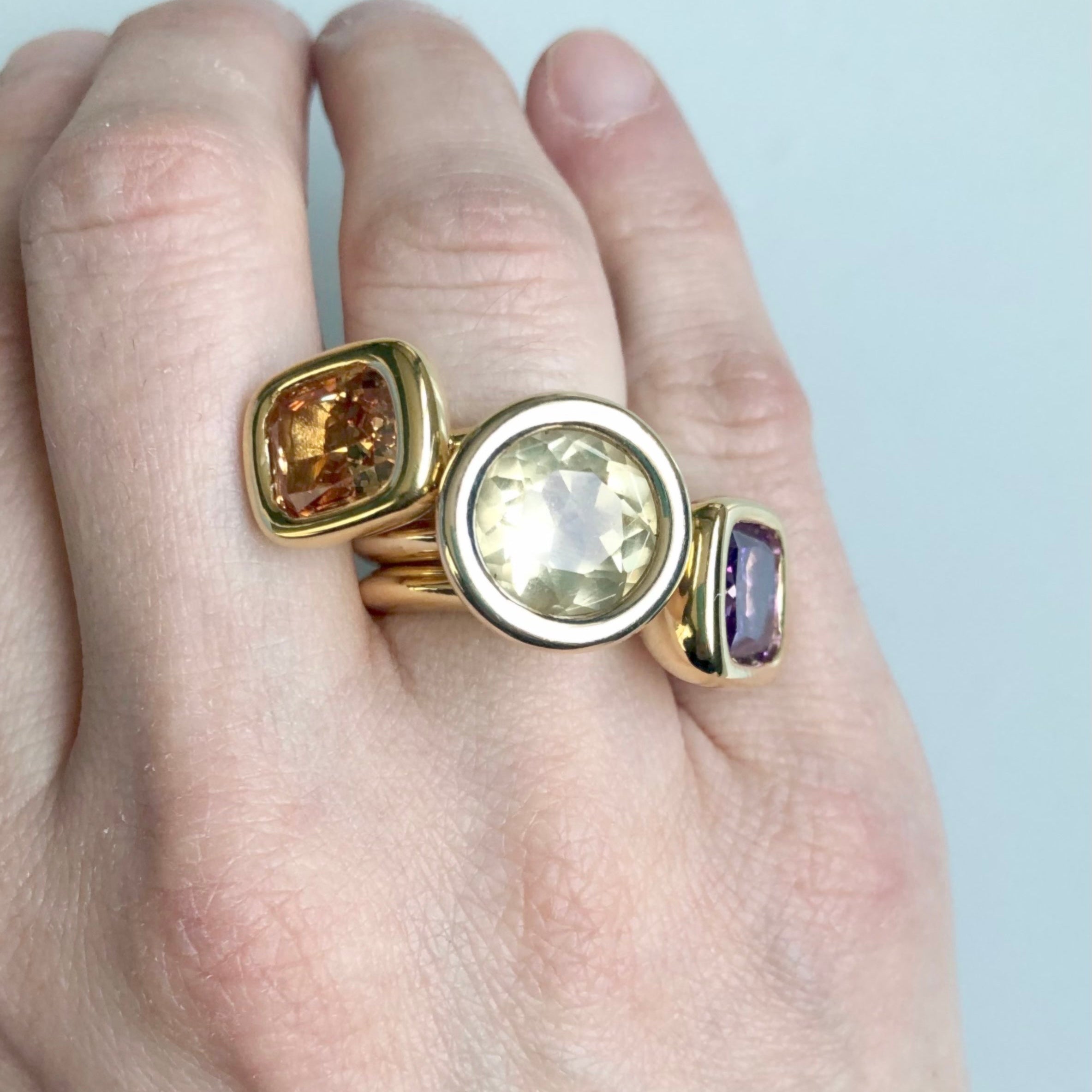 Gold ring with gemstones on a hand against a light background