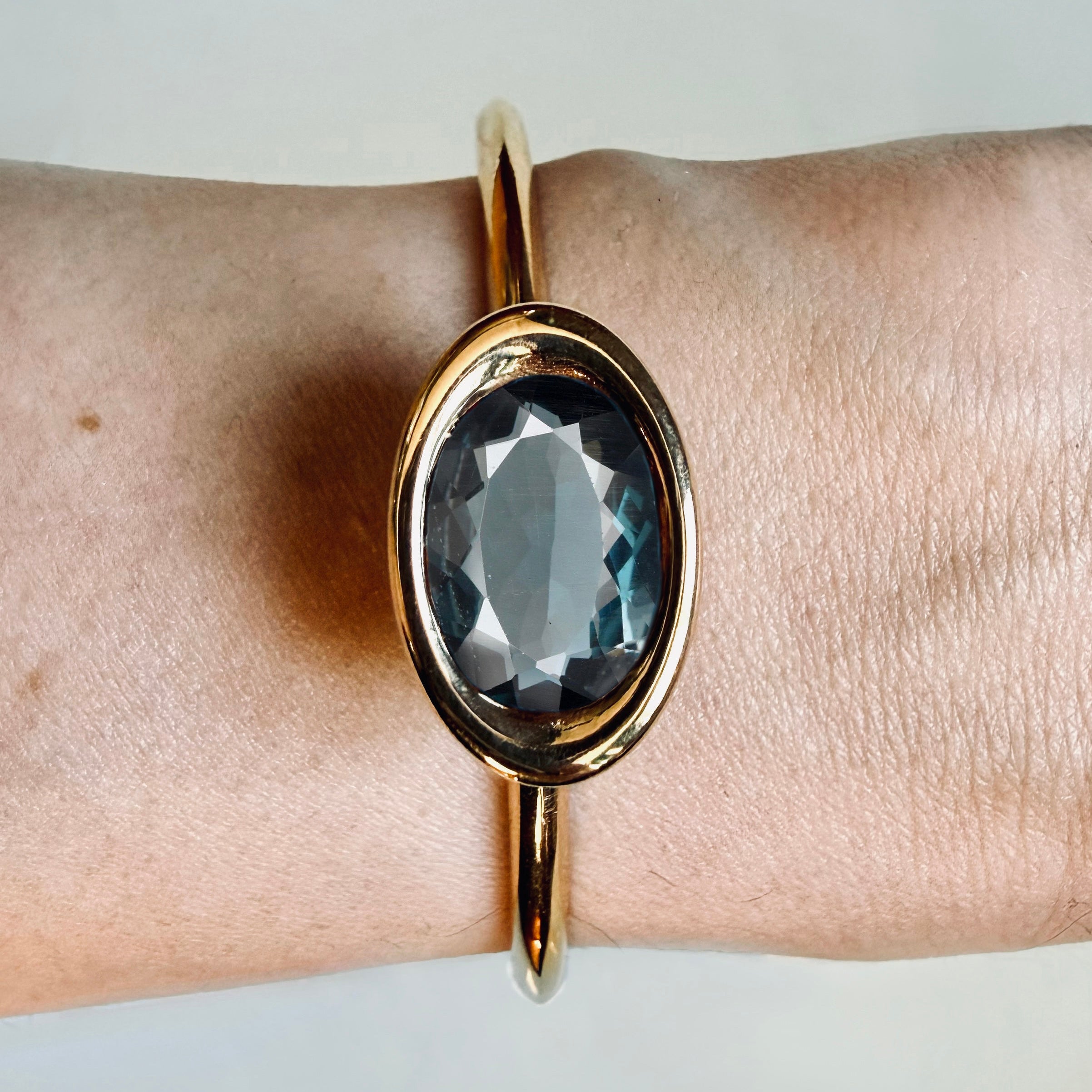 Gold bracelet with a large blue gemstone on a wrist against a neutral background