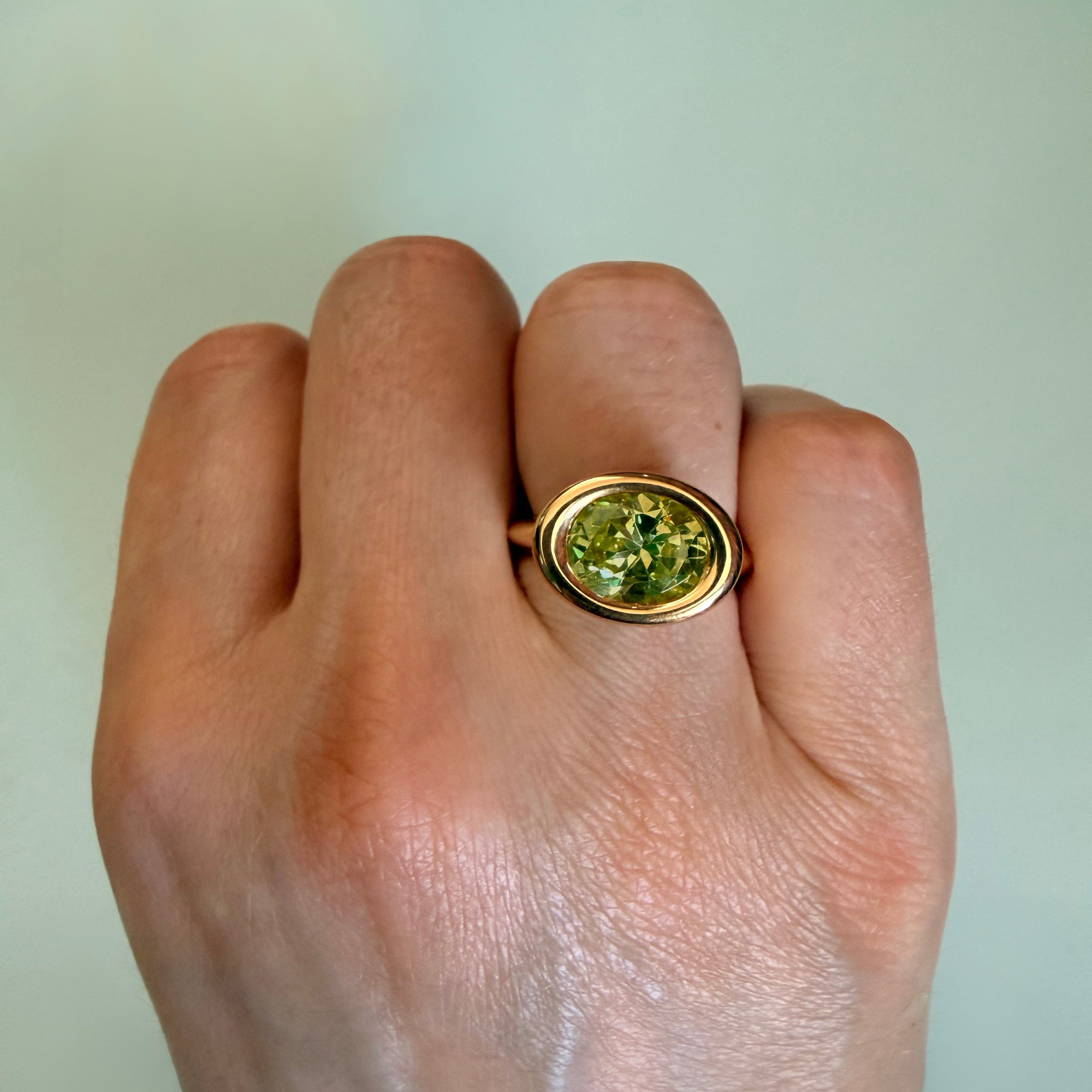 Hand wearing a gold ring with a green gemstone on a plain background
