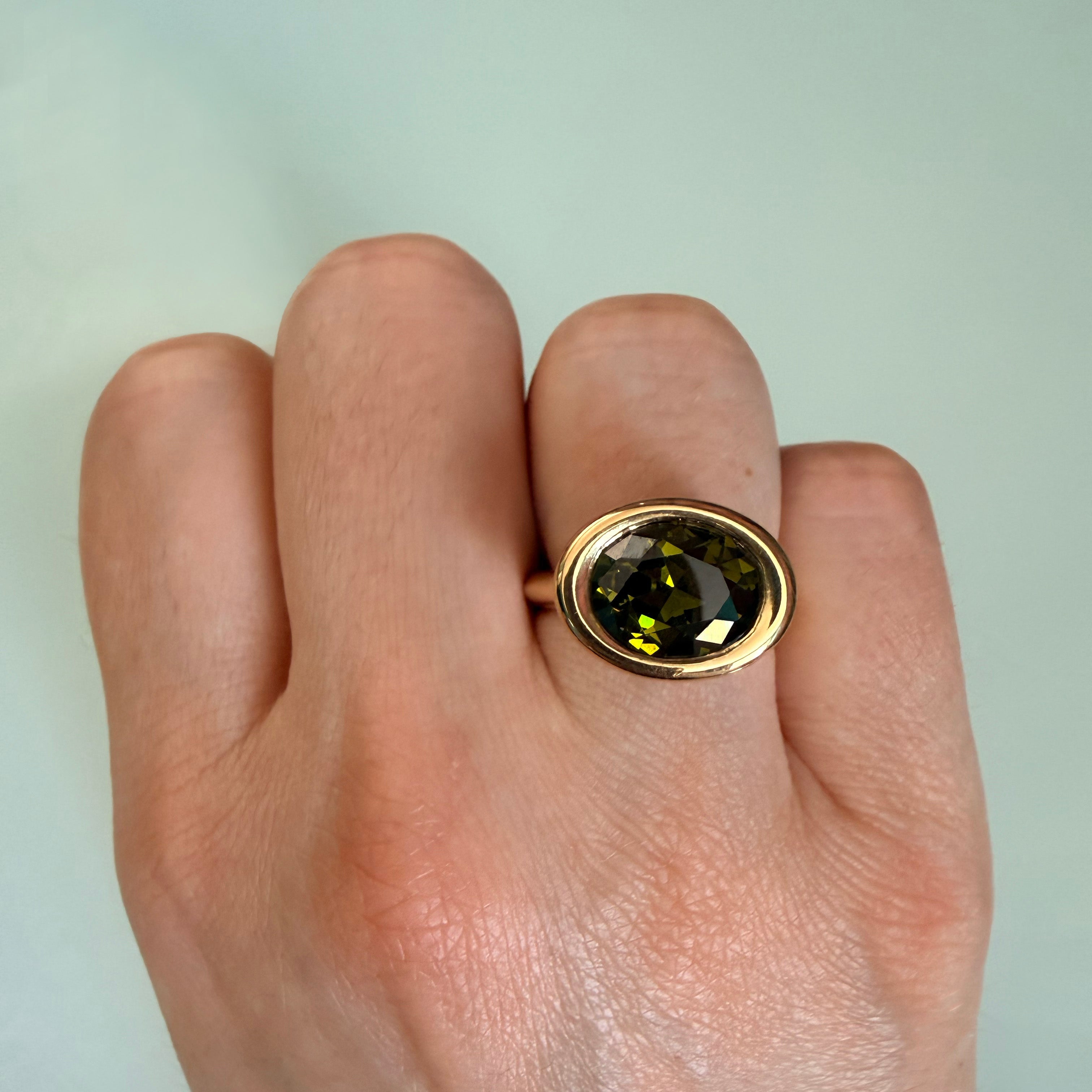 Gold ring with a green gemstone on a person's finger against a light background