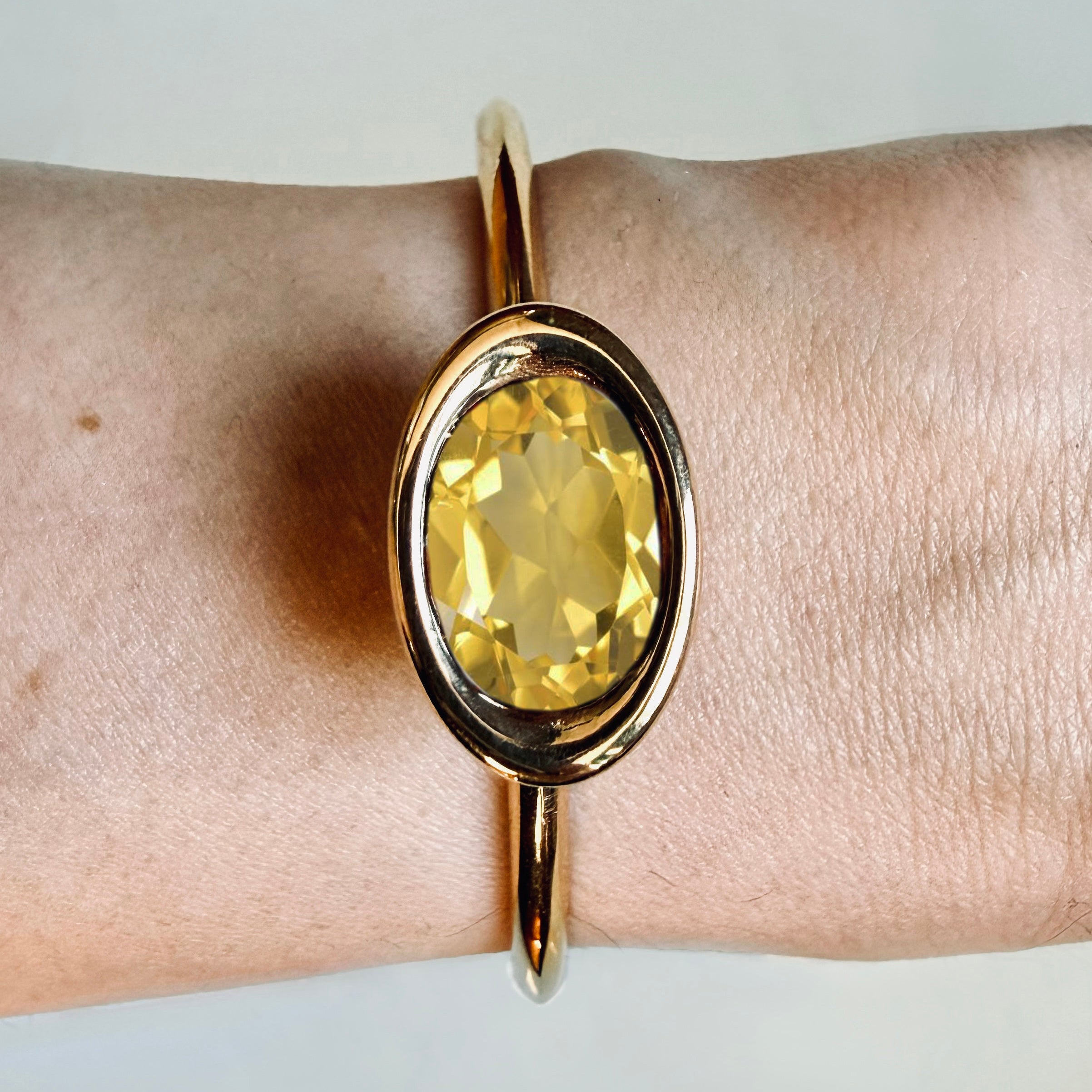 Gold bracelet with a yellow gemstone on a wrist against a neutral background